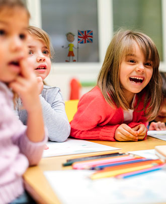 3 élèves de maternelle qui rigolent autour d'une table lors d'un cours d'anglais avec Acadomia